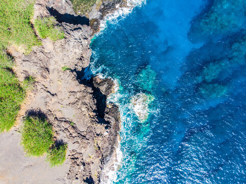 Vue aérienne verticale d'un littoral tropical dans l'océaen Indien avec écume sur l'eau à flanc de falaise, La Réunion © Attraction