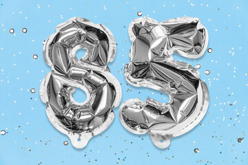 Silver foil balloon number, digit eighty five on a blue background with sequins. Birthday greeting card with inscription 85. Anniversary concept. Numerical digit. Celebration event, template.