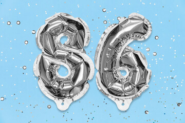 Silver foil balloon number, digit eighty six on a blue background with sequins. Birthday greeting card with inscription 86. Top view. Numerical digit. Celebration event, template.
