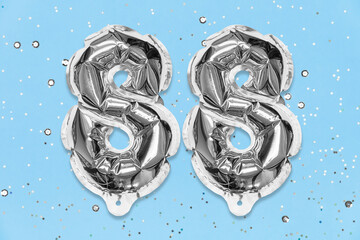 Silver foil balloon number, digit eighty eight on a blue background with sequins. Birthday greeting card with inscription 88. Top view. Numerical digit. Celebration event, template.