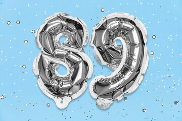 Silver foil balloon number, digit eighty nine on a blue background with sequins. Birthday greeting card with inscription 89. Top view. Numerical digit. Celebration event, template.