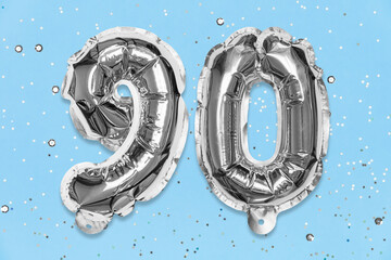 Silver foil balloon number, digit ninety on a blue background with sequins. Birthday greeting card...