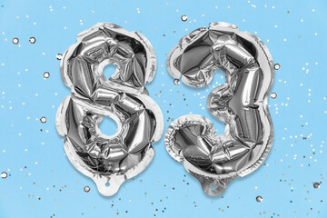 Silver foil balloon number, digit eighty three on a blue background with sequins. Birthday greeting card with inscription 83. Top view. Numerical digit. Celebration event, template.