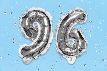 Silver foil balloon number, digit ninety six on a blue background with sequins. Birthday greeting card with inscription 96. Top view. Numerical digit. Celebration event, template.