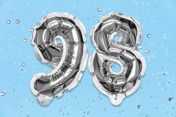 Silver foil balloon number, digit ninety eight on a blue background with sequins. Birthday greeting card with inscription 98. Top view. Numerical digit. Celebration event, template.