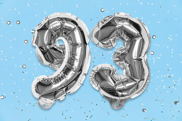 Silver foil balloon number, digit ninety three on a blue background with sequins. Birthday greeting card with inscription 93. Top view. Numerical digit. Celebration event, template.
