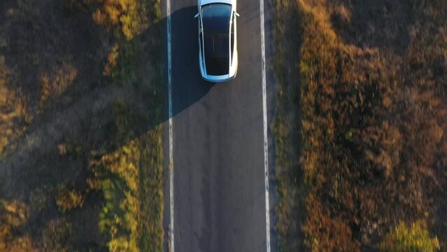 Aerial shot of electrical car driving on country road at summer evening. New SUV vehicle speeding through highway. Ecology friendly car riding on electric charge along motorway. Top view Close up