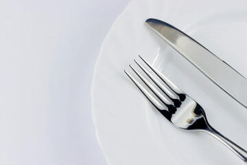 Top view of silver fork and knife on the plate over white background