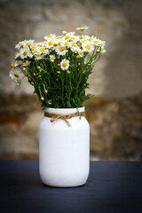 Vintage handmade vase with chamomile flowers on wooden table
