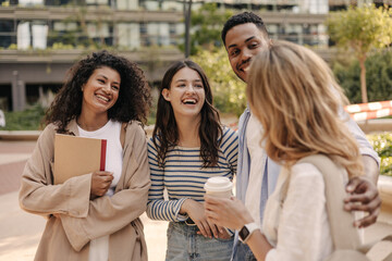Young interracial friends with good mood met after outdoor lessons in afternoon. Guy and girls wear casual clothes spring. Concept of enjoying moment
