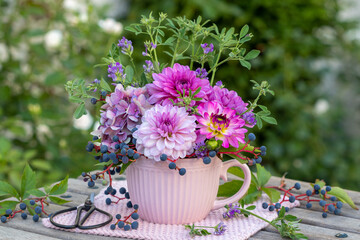 Blumenstrauß mit pink und lila Dahlien, Hortensien-Blüten und Beeren des Wilden Wein in Tasse im Garten