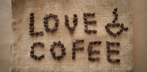 Inscription love coffee from coffee beans on burlap background. Mockup for cafe or coffee shop advertising in rustic style.