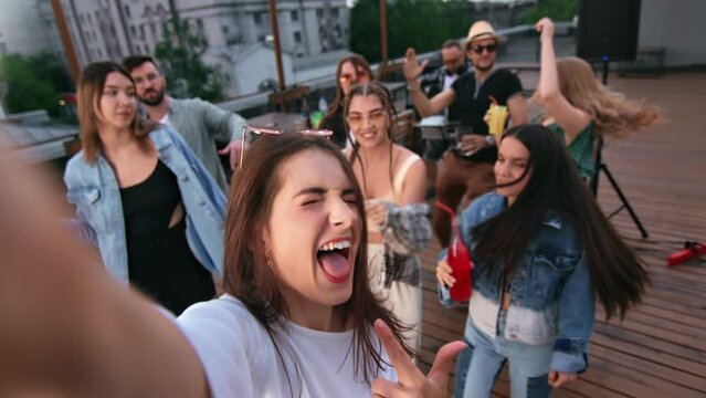 Woman blogger vlogger shooting POV selfie video photo at roof party smiling dancing with friends