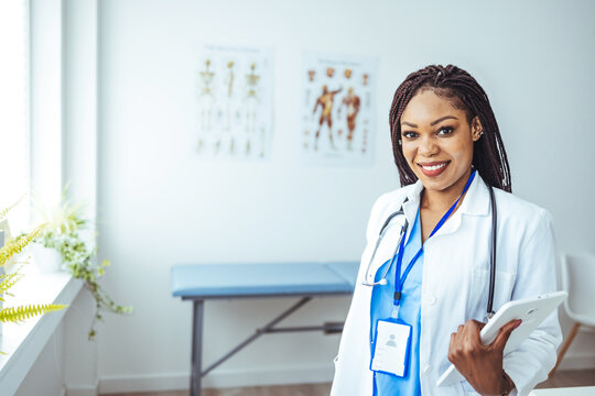Portrait of confident smiling female doctor. Mid adult medical professional is wearing lab coat and stethoscope. She is standing against gray wall in hospital. 
