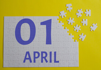 1 april calendar date on a white puzzle with separate details. Puzzle on a yellow background with a blue inscription