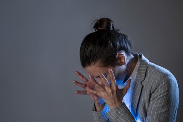 Stress at work and professional burnout. young woman in a business suit standing clutching head, portrait on a gray background