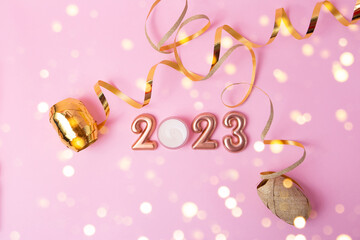 Top view of rose gold numbers 2023 on pink background.Festive confetti and sparlks around.