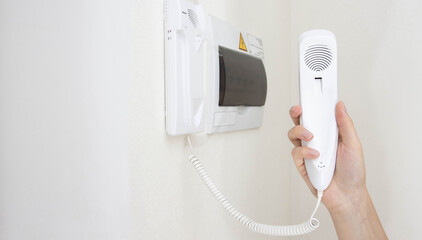 Intercom handset in a man's hand against the background of a white wall in the room. Security from unauthorized persons and theft in the apartment. Copy space for text