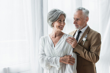 bearded middle aged groom in suit touching shoulder of cheerful bride in white dress