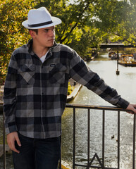 Young hipster wearing a white hat posing in front of a river walk.