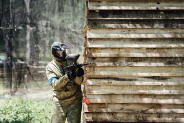 Fototapeta premium Paintball player shooting with marker from behind the wall during the paintball game