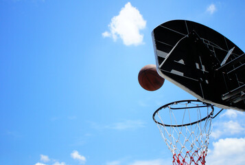 Outdoor basketball shoot into the red and white net where the hoop is under the beautiful cloud and blue sky.