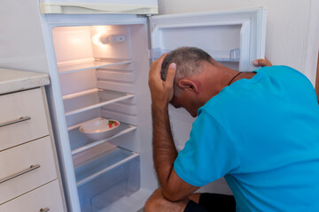 Man looking for food in the refrigerator. Concept of rising food prices, of impoverishment of the poor.