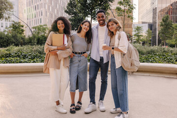 Fototapeta premium In full growth, good young classmates of caucasian, african appearance spend leisure time together on street. Guy and girls wear casual clothes to study. Relax, lifestyle concept