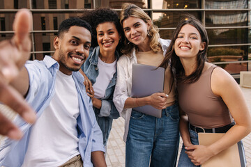 Nice young interracial students taking selfie relaxing at recess near college during day. Guy and...
