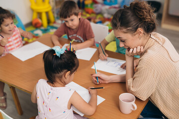 children drawing with teacher assistance in day care - obrazy, fototapety, plakaty