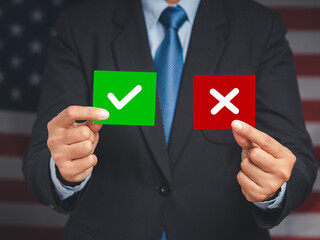Close-up of hands businessman in a suit holding two papers with a checkmark and cross while standing on the American flag background