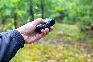 Forest navigator in the forest in a man's hand against the background of green trees. The concept of orienteering in order not to get lost in the forest. Copy space for text