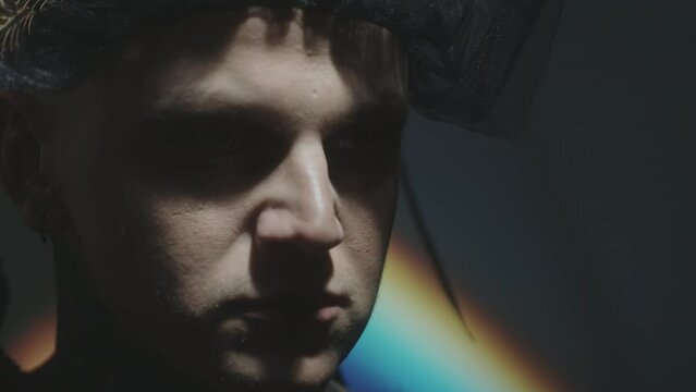 Close up shot of dramatic man taking off black gothic veil in dark studio with low key lighting and rainbow light projection
