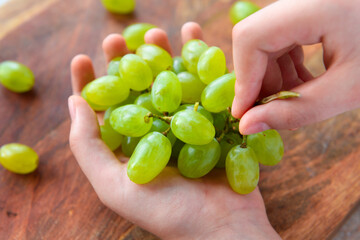 a woman's hand with green grapes, wooden background, concept of fresh sweet fruits and healthy food