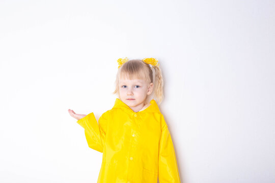 Little girl aged 3 years in a yellow raincoat on a white background. The concept of bad weather and autumn. Copy space for text