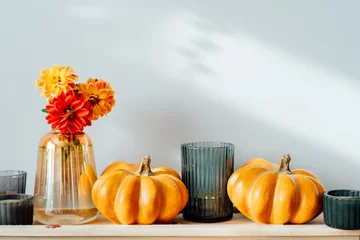 Deurstickers Autumn, fall cozy composition. Orange pumpkins, candles, dahlia flowers in vase on the wooden tray on the table with white wall background. Scandinavian minimalist hygge home decor. Selective focus © okrasiuk