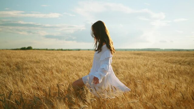 beautiful young woman with dark loose hair is walking alone on ripe wheat field in summer, slow motion