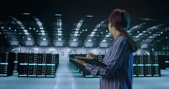 A young female using tablet while working in server room in contemporary data center.