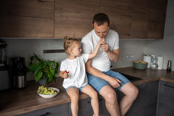 Cute little girl and her handsome dad are eating fruit in modern kitchen. Healthy eating.