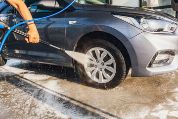 A man washes the wheels on his car at a self-service car wash using a hose with pressurized water