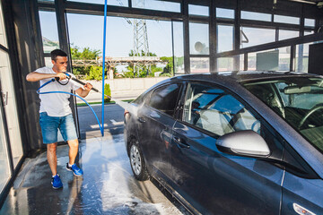 A man washes his car at a self-service car wash using a hose with pressurized water