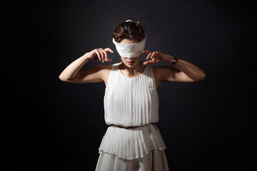 Fototapeta na wymiar An antique heroine blindfolded, a young woman in a tunic with a blindfold, a contrasting close-up portrait on a black background