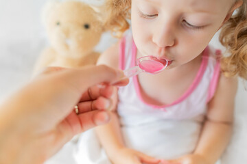 The child drinks syrup from a measuring spoon. Treatment at home.
