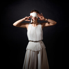 Close your eyes, hide from the truth, concept. An ancient heroine blindfolded, a young woman in a tunic with a blindfold, covers her face with her hands
