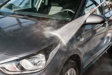 A man washes his car at a self-service car wash using a hose with pressurized water