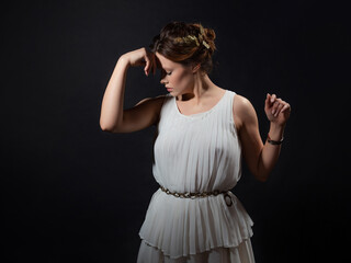 An ancient heroine, a young woman in the image of an ancient Greek goddess or muse. A noble heroine in a white tunic and a laurel wreath, a full-length photo on a black background