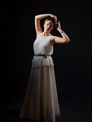 An ancient heroine, a young woman in the image of an ancient Greek goddess or muse. A noble heroine in a white tunic and a laurel wreath, a full-length photo on a black background