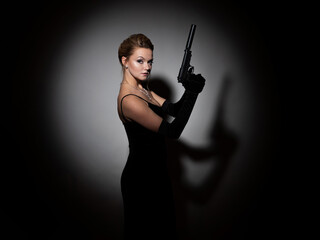 A dangerous spy. A femme fatale in a black dress with an open back holds a pistol with a silencer...