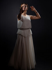 An ancient heroine, a young woman in the image of an ancient Greek goddess or muse. A noble heroine in a white tunic and a laurel wreath, dancing on a black background