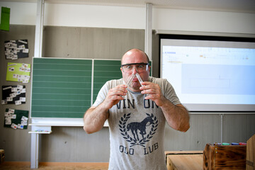 A crazy chemistry teacher in goggles sniffs reagents from a test tube.